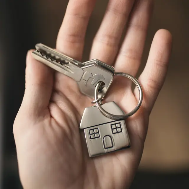 An open hand holding a door key on a keyring.